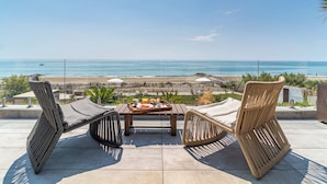 A terrace with wicker furniture, a table with breakfast items, and a view of the beach and ocean. - Villa Miramar (Frontignan)