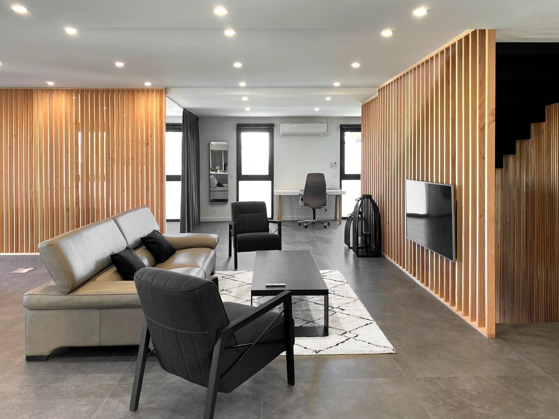 A modern office space with a sofa, chairs, a coffee table, a TV, and wooden paneling.