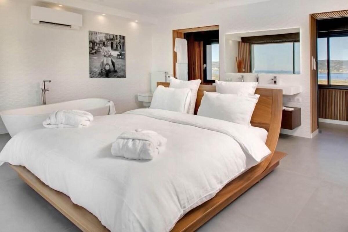 A modern hotel room with a large bed, a bathtub, and a view of the sea.