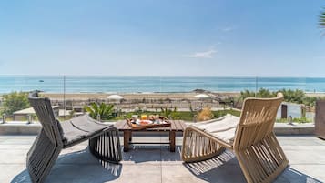 A terrace with wicker furniture, a table with breakfast items, and a view of the beach and ocean.