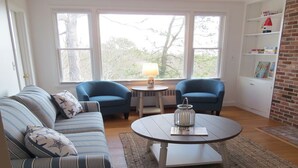 Ein Wohnzimmer mit einem gestreiften Sofa, zwei blauen Sesseln, einem runden Couchtisch und einem kleinen Tisch mit einer Lampe.
