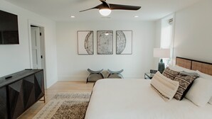 A bedroom with a bed, a ceiling fan, a nightstand, and wall art.