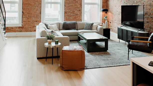 A spacious living room with a brick wall, large windows, a sofa set, a coffee table, and a TV.