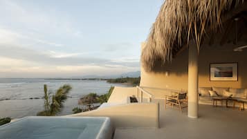 A poolside area with a view of the ocean, a thatched roof, and a seating area with a sofa and chairs.