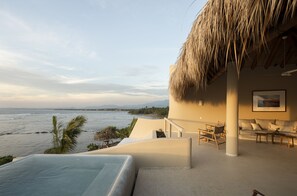 Uma área na piscina com vista para o mar, um telhado de palha e um espaço de estar com sofá e cadeiras.