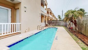 Une piscine située à côté d’un immeuble doté de balcons, d’une clôture en bois et de palmiers.