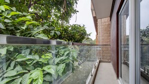 Un balcon doté d’une balustrade en verre, offrant une vue sur une végétation luxuriante et un mur de pierre.