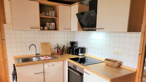 A compact kitchen with white cabinets, a stainless steel sink, a black stove, and a coffee maker. - New! Haus Seebrise - at Useriner See - Müritz National Park (Userin)