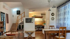 Un vaste espace de vie comprenant une table à manger en bois, un escalier et une cuisine en arrière-plan.