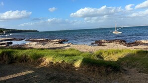 Un paysage côtier avec des rivages rocheux, des zones herbeuses et un voilier sur l’eau.