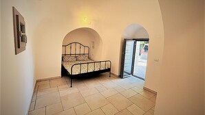 Een slaapkamer met een bed, een gewelfde deuropening en een betegelde vloer.