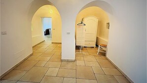 Een gang met betegelde vloer, witte muren en twee gewelfde deuropeningen naar een andere kamer.
