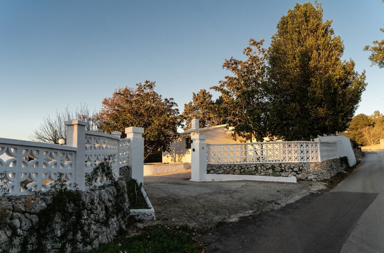 A gated entrance with a white fence and stone wall, leading to a building with a stone foundation and a white exterior.