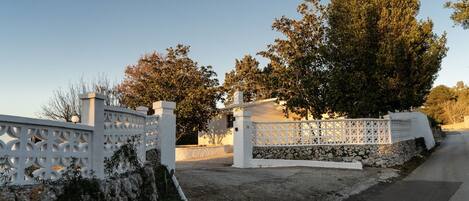 A gated entrance with a white fence and stone wall, leading to a building with a stone foundation and a white exterior.