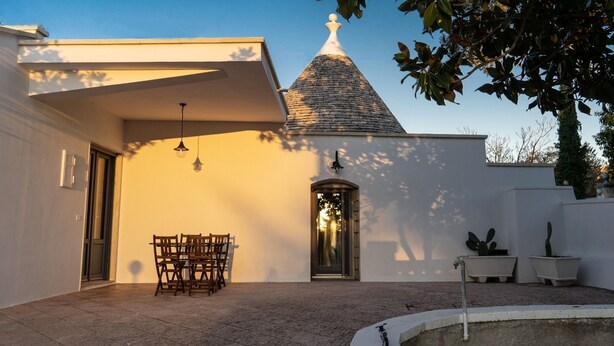 Een modern gebouw met een witte gevel, een pannendak en een kleine tuin met een tafel en stoelen.