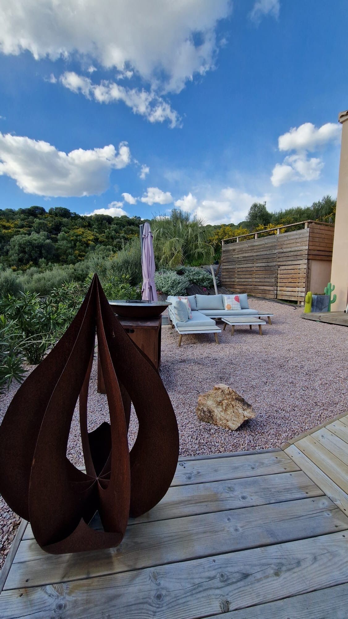 A patio with a metal sculpture, a sofa, and a table set on a gravel surface.