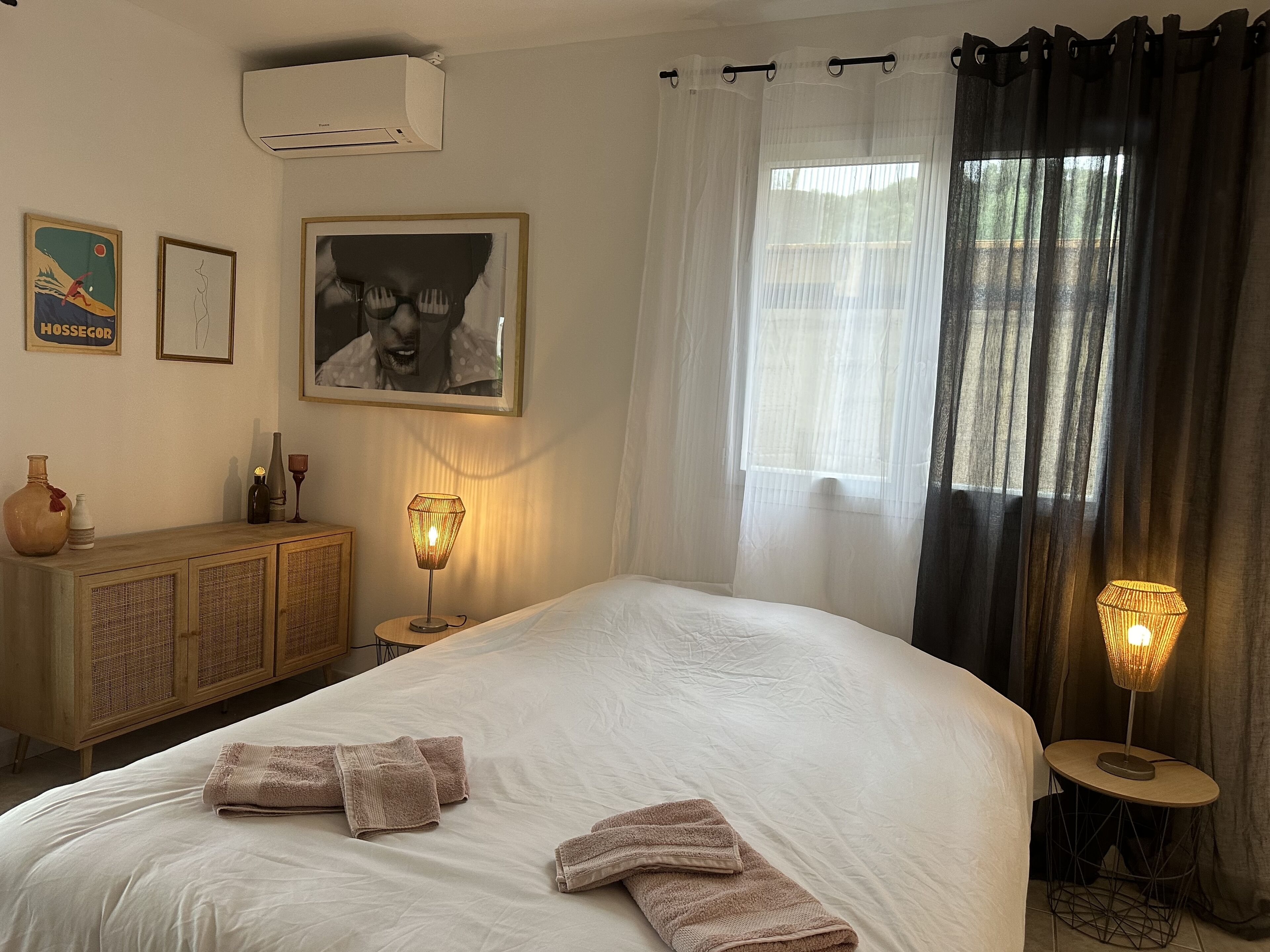 Une chambre d’hôtel avec un grand lit, deux lampes de chevet, une armoire en bois et une fenêtre ornée de rideaux légers.