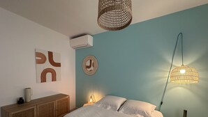 Un dormitorio con una cama, una lámpara de noche, aire acondicionado instalado en la pared y un adorno en la pared.