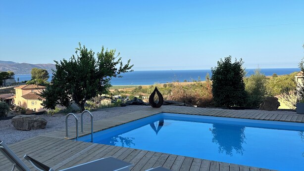 Terraza de madera con piscina, sillas de descanso y vista al mar.