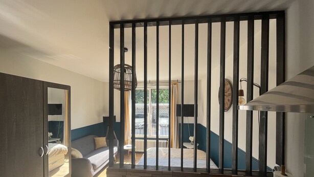 A room with a bed, a dresser, a mirror, a window with curtains, and a staircase. - Studio LA Fregate - Proche Centre Lorient (Lorient)