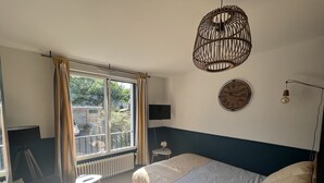 A bedroom with a bed, a window with curtains, a wall clock, a mounted TV, and a hanging light fixture. - Studio LA Fregate - Proche Centre Lorient (Lorient)