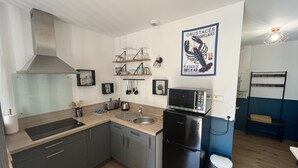 A compact kitchen with a stainless steel range hood, a microwave, and a refrigerator. There are wooden cabinets, a sink, and a shelf with kitchen utensils. A poster of a lobster is on the wall. - Studio LA Fregate - Proche Centre Lorient (Lorient)