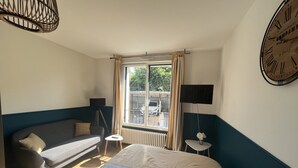 A bedroom with a bed, a sofa, a small table, a TV, and a window with curtains. - Studio LA Fregate - Proche Centre Lorient (Lorient)