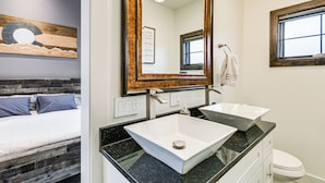 Ein modernes Badezimmer mit zwei Waschbecken, einem großen Spiegel und einem Bett mit einem Holz-Kopfstück.