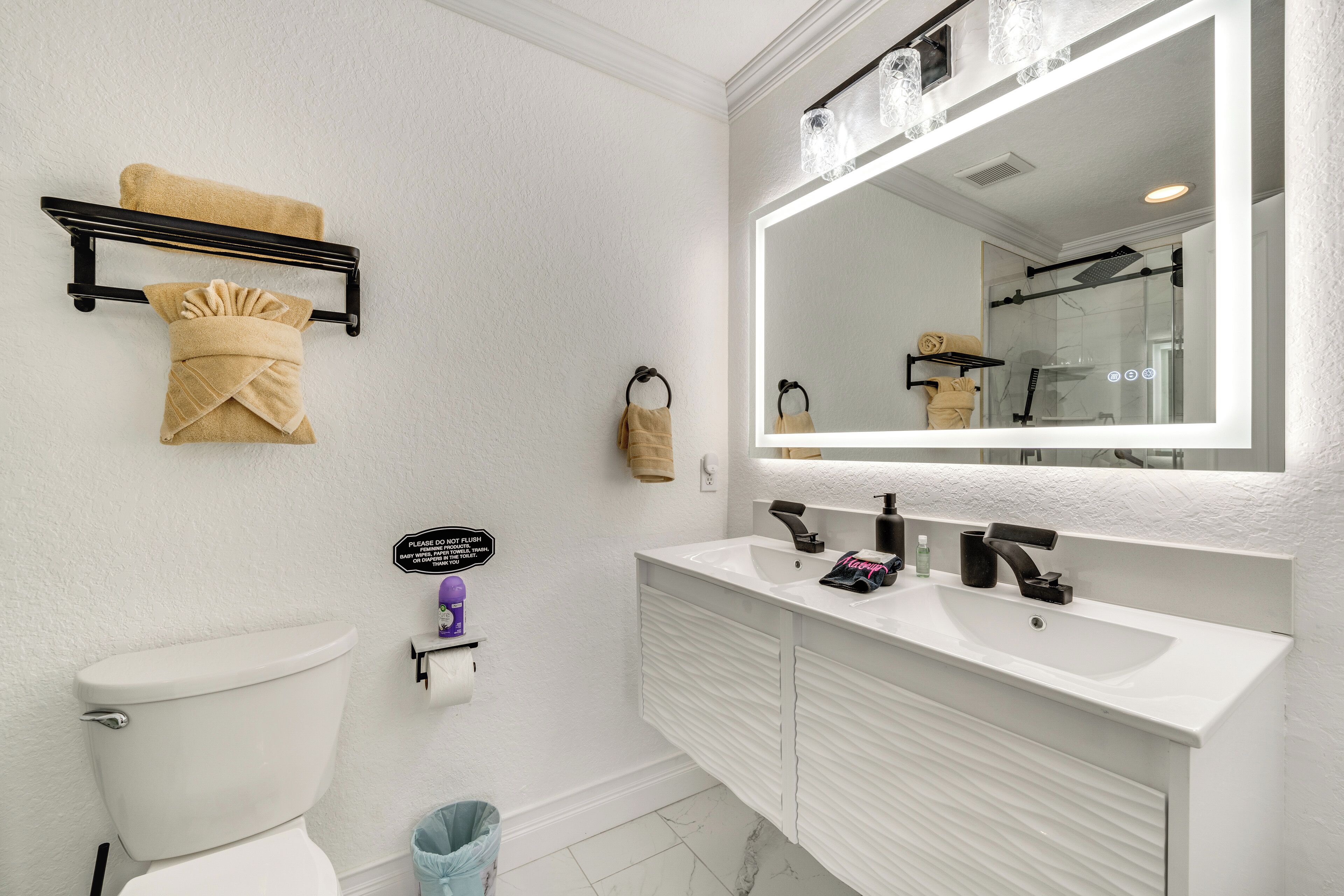 Een badkamer met een wit toilet, een wastafel met spiegel erboven en een handdoekrek met handdoeken.