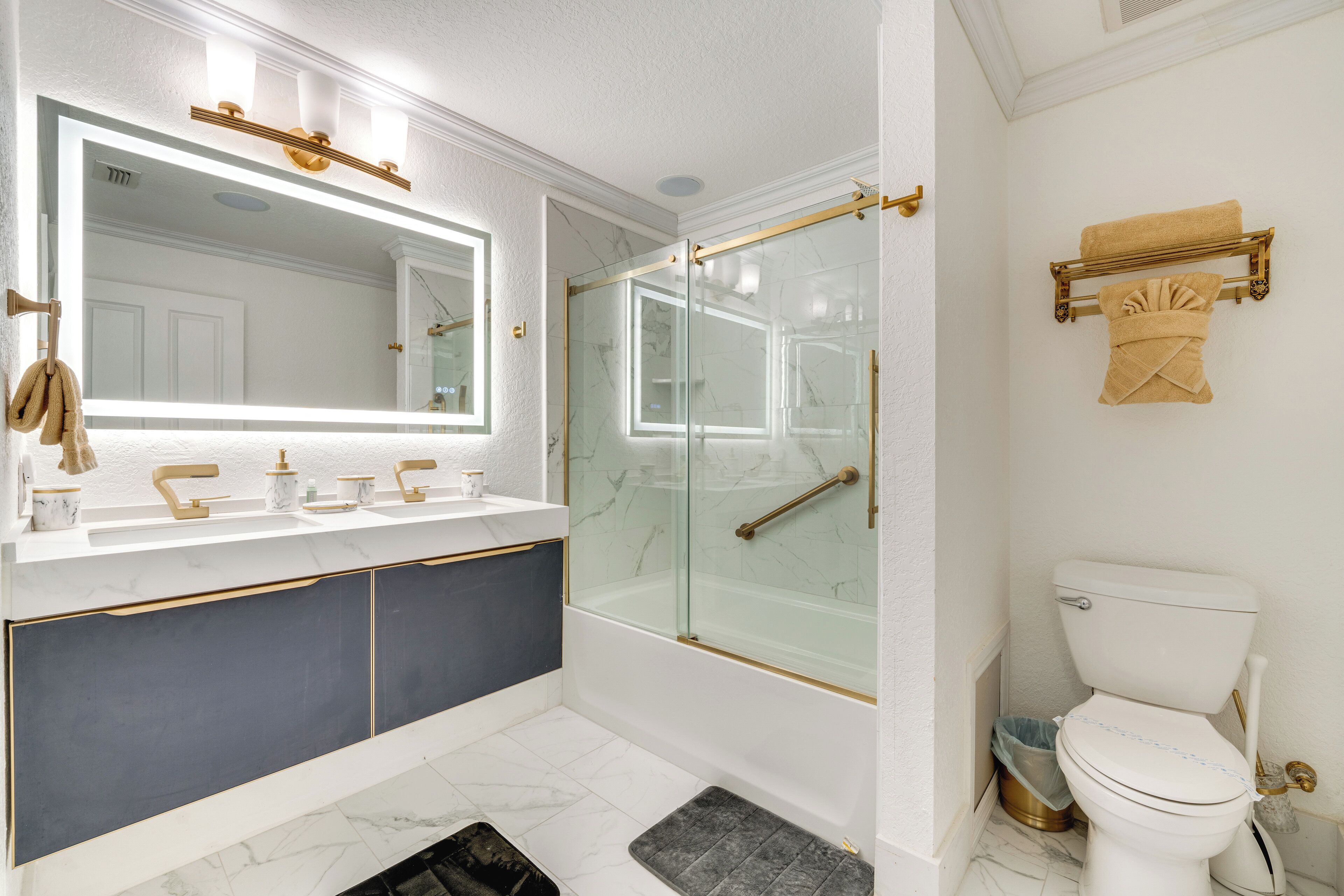 A modern bathroom with a glass-enclosed shower, a white toilet, and a vanity with gold fixtures.