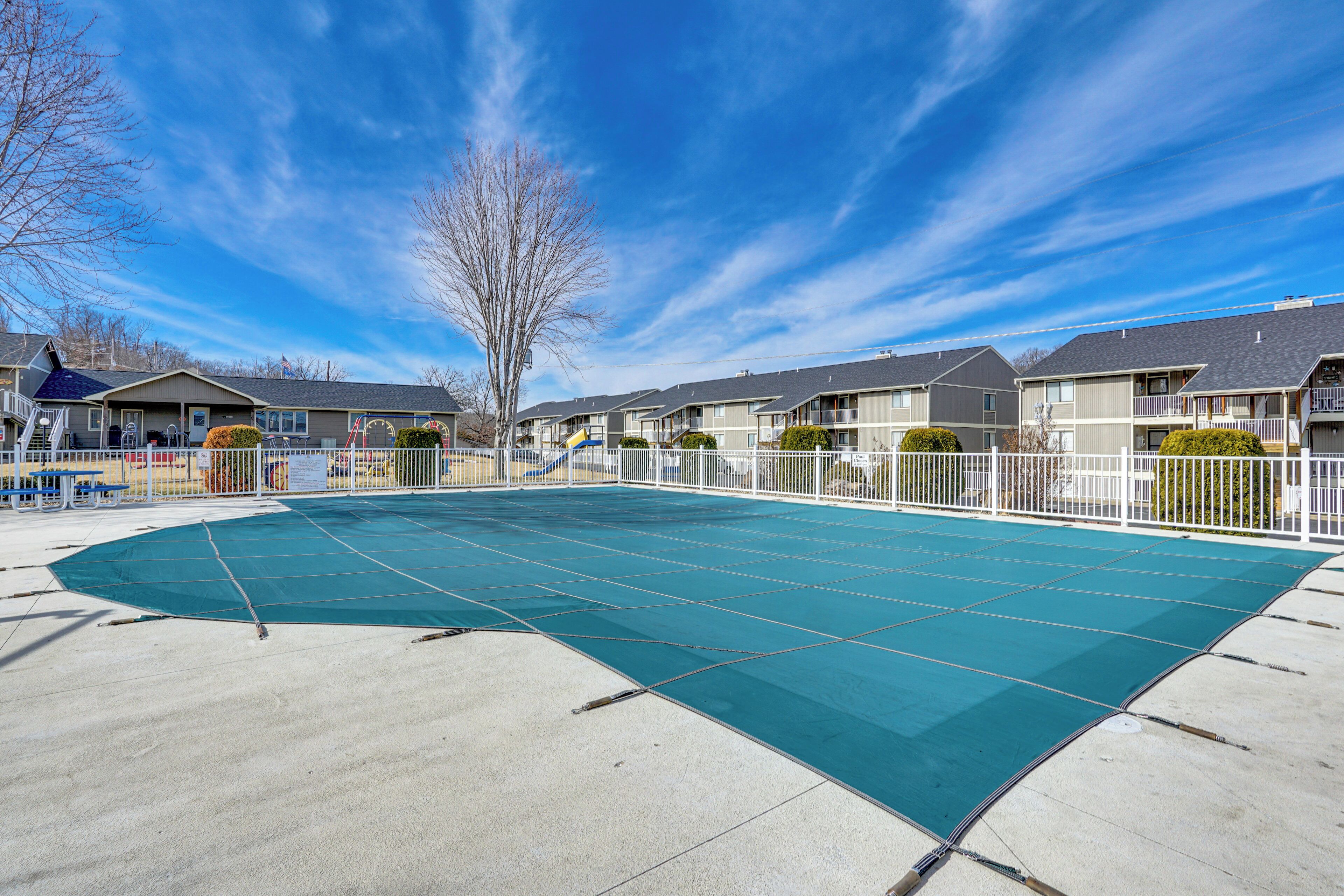 A swimming pool with a blue deck, surrounded by a white fence, and adjacent to a row of townhouses.