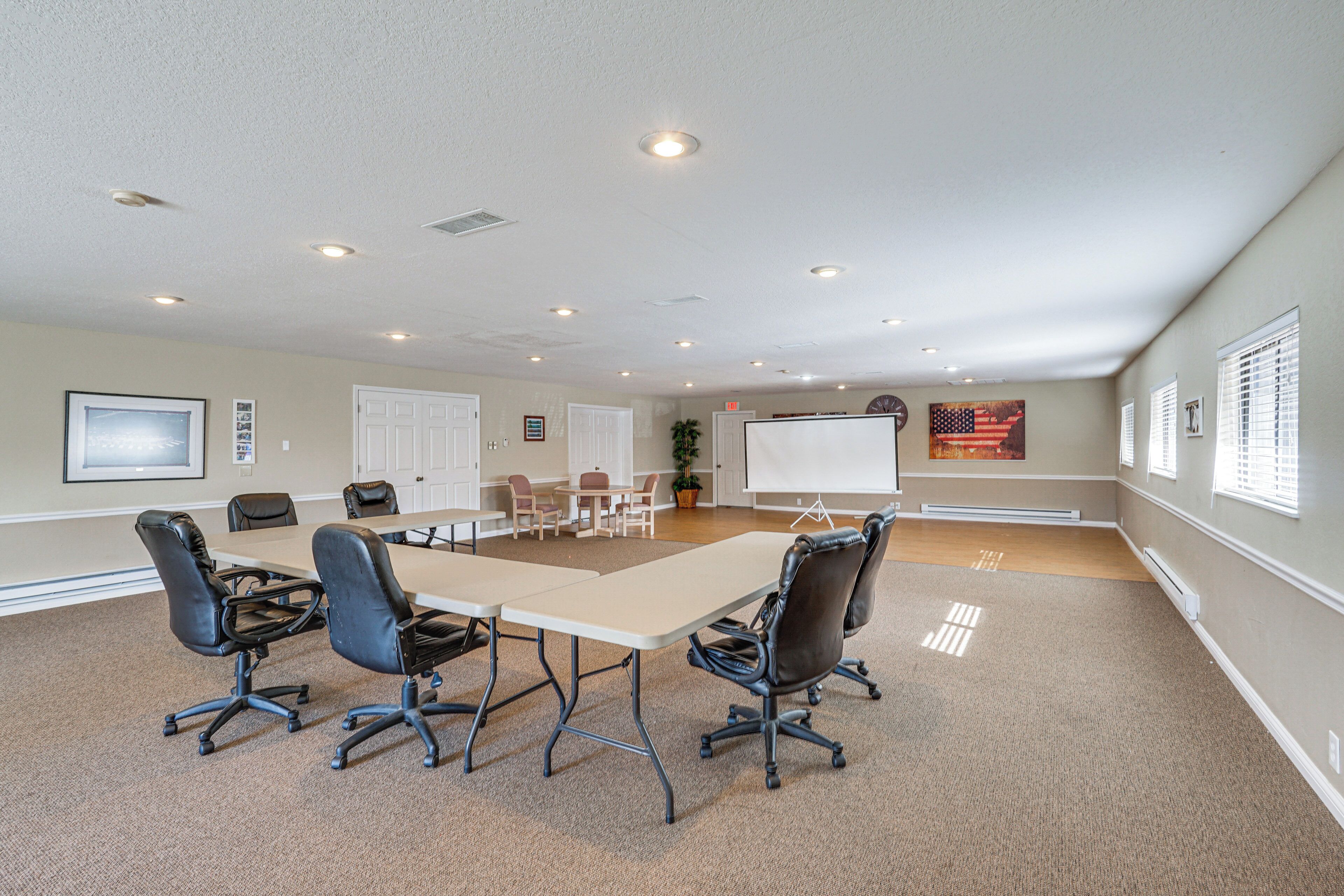 A conference room with a long table, four chairs, a projector screen, and a whiteboard.