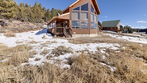 A wooden cabin with large windows, a porch, and a view of a snowy landscape. - Cozy Duck Creek Village Cabin w/ Hot Tub & Views! (Duck Creek Village)
