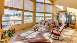 A spacious living room with large windows, a sofa, a rocking chair, and a dining area. - Cozy Duck Creek Village Cabin w/ Hot Tub & Views! (Duck Creek Village)