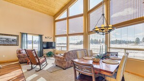 A spacious living room with a wooden ceiling, large windows, a fireplace, and a dining area with a wooden table and chairs. - Cozy Duck Creek Village Cabin w/ Hot Tub & Views! (Duck Creek Village)