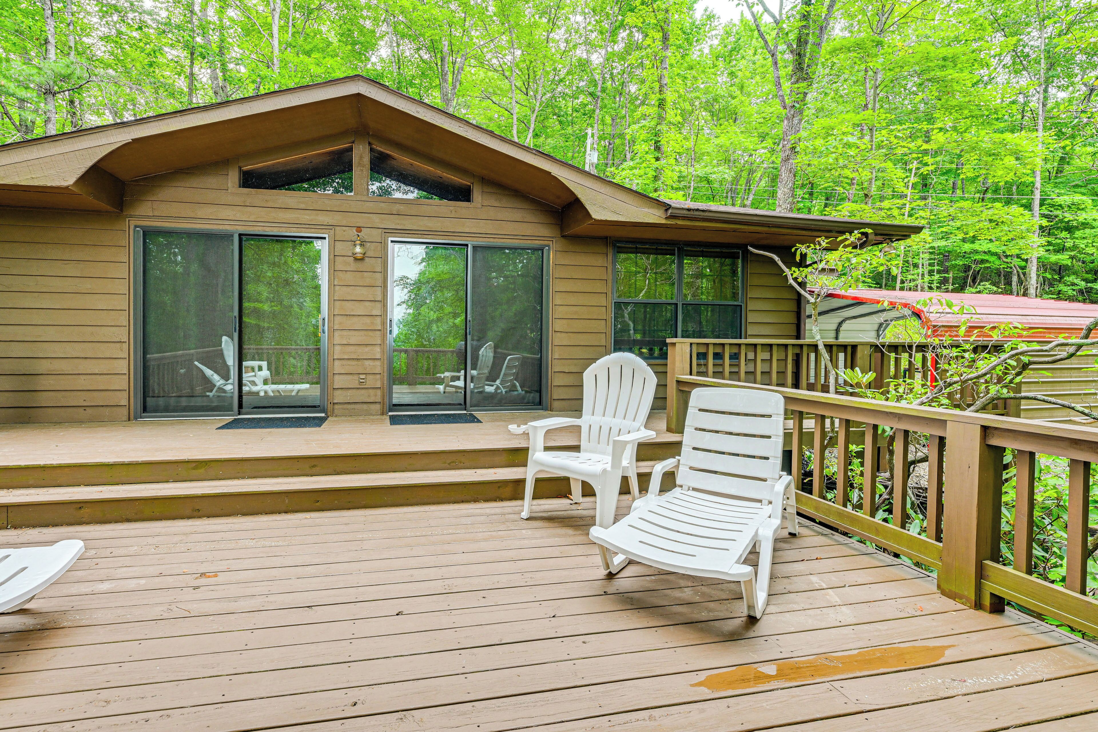 A wooden deck with two white chairs and a bench, overlooking a forested area.