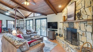 A spacious living room with a stone fireplace, a large TV, and a cozy seating area with a sofa and chairs. - Smoky Mountain Cabin w/ Fire Pit & Stunning Views! (Andrews)