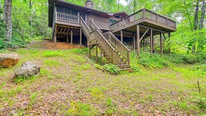 A wooden cabin with a deck and staircase, surrounded by dense forest. - Smoky Mountain Cabin w/ Fire Pit & Stunning Views! (Andrews)