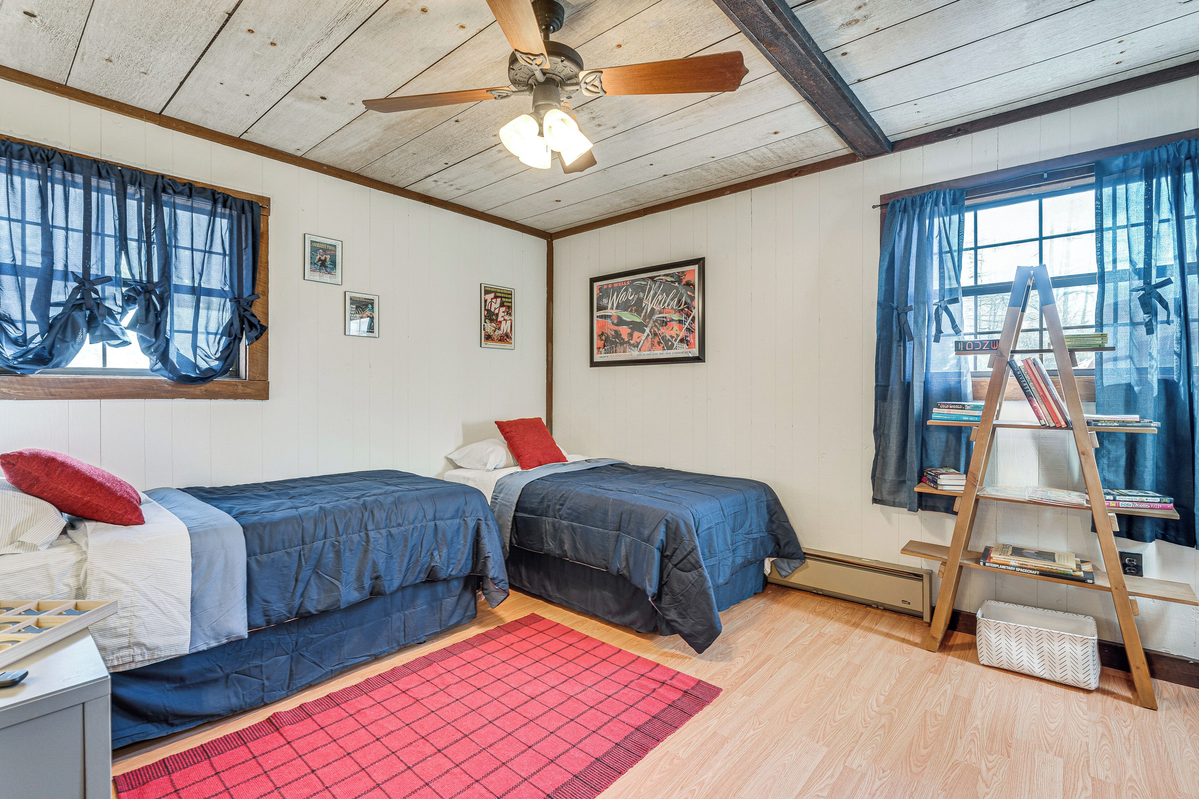 A bedroom with two beds, a ceiling fan, a ladder, and a window with curtains.