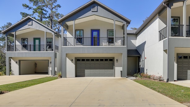 A two-story residential building with a central garage, a covered front porch, and a second-story balcony. - Near WEC & Golf! Ocala Townhome w/ EV Charger (Ocala)