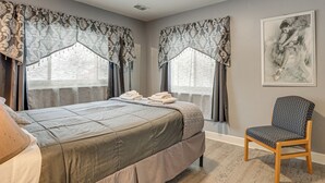 A bedroom with a bed, two windows with curtains, a chair, and a painting on the wall. - Kalamazoo Vacation Rental Near Golf & Parks! (Kalamazoo)
