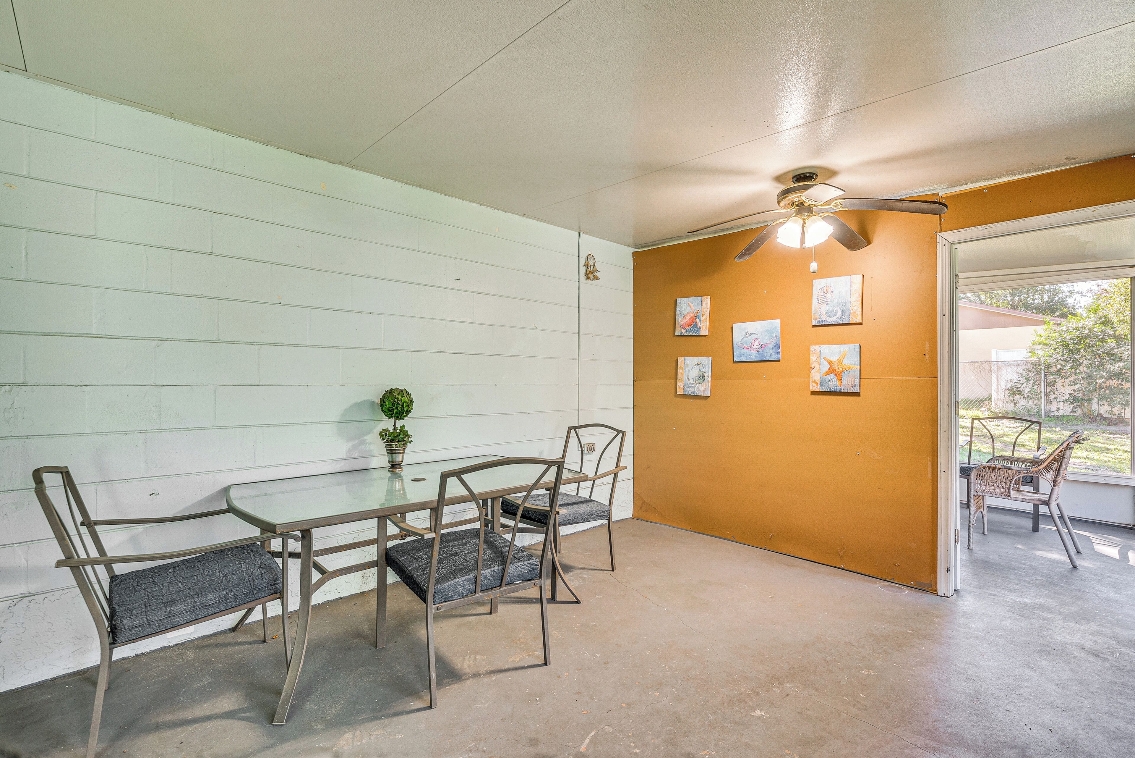 A dining area with a glass table and metal chairs, a ceiling fan, and artwork on the walls.