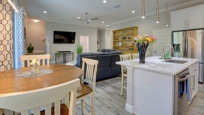 A modern kitchen with white cabinetry, a central island, and a dining area with a wooden table and chairs. - Modern Ocala Townhome w/ EV Charger Near WEC (Ocala)