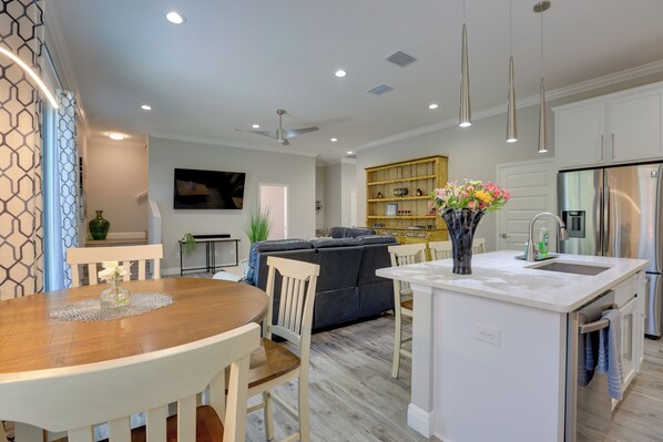 Een moderne keuken met witte kasten, een centraal eiland en een eethoek met een houten tafel en stoelen.