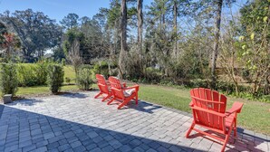 A paved patio with red Adirondack chairs and a view of a wooded area. - Modern Ocala Townhome w/ EV Charger Near WEC (Ocala)