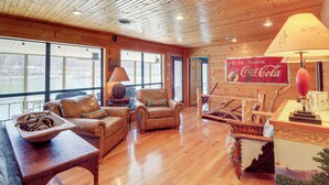 A cozy cabin interior with wooden floors, leather furniture, and large windows offering a view of the outdoors. - Please Note: No Boat Slip Available for Dock (Flippin)