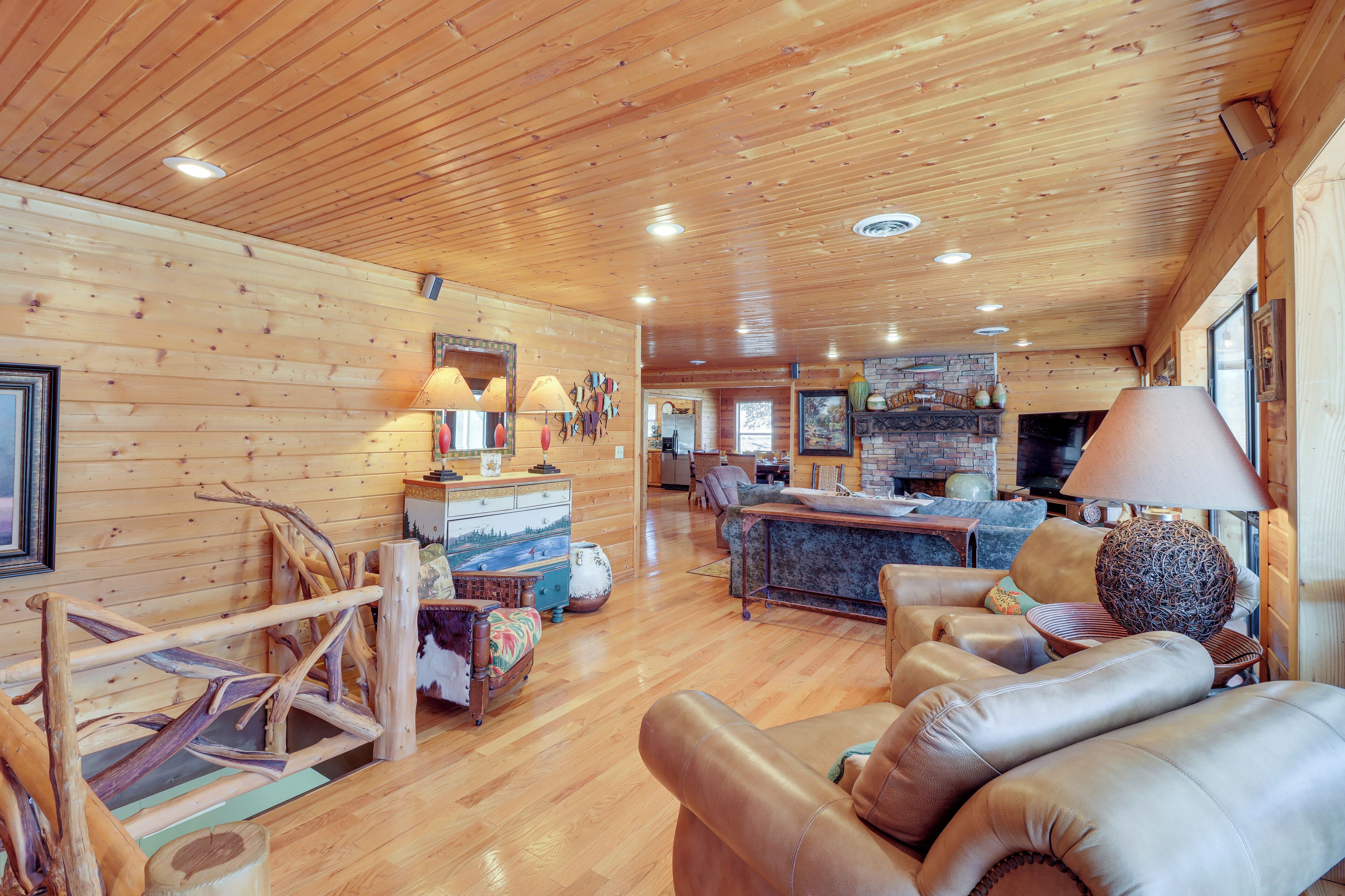 A spacious living area with wooden walls and ceiling, a fireplace, and a dining area with a bar.