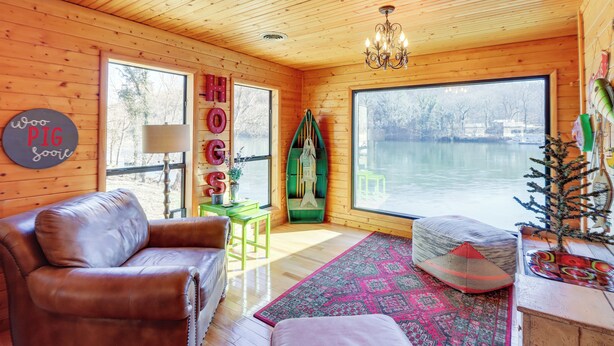 A cozy cabin with a large window overlooking a lake, a leather sofa, a patterned rug, and a wooden ceiling. - Please Note: No Boat Slip Available for Dock (Flippin)