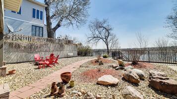 A patio with red Adirondack chairs, a brick pathway, and a rocky garden area with large rocks and a small tree.