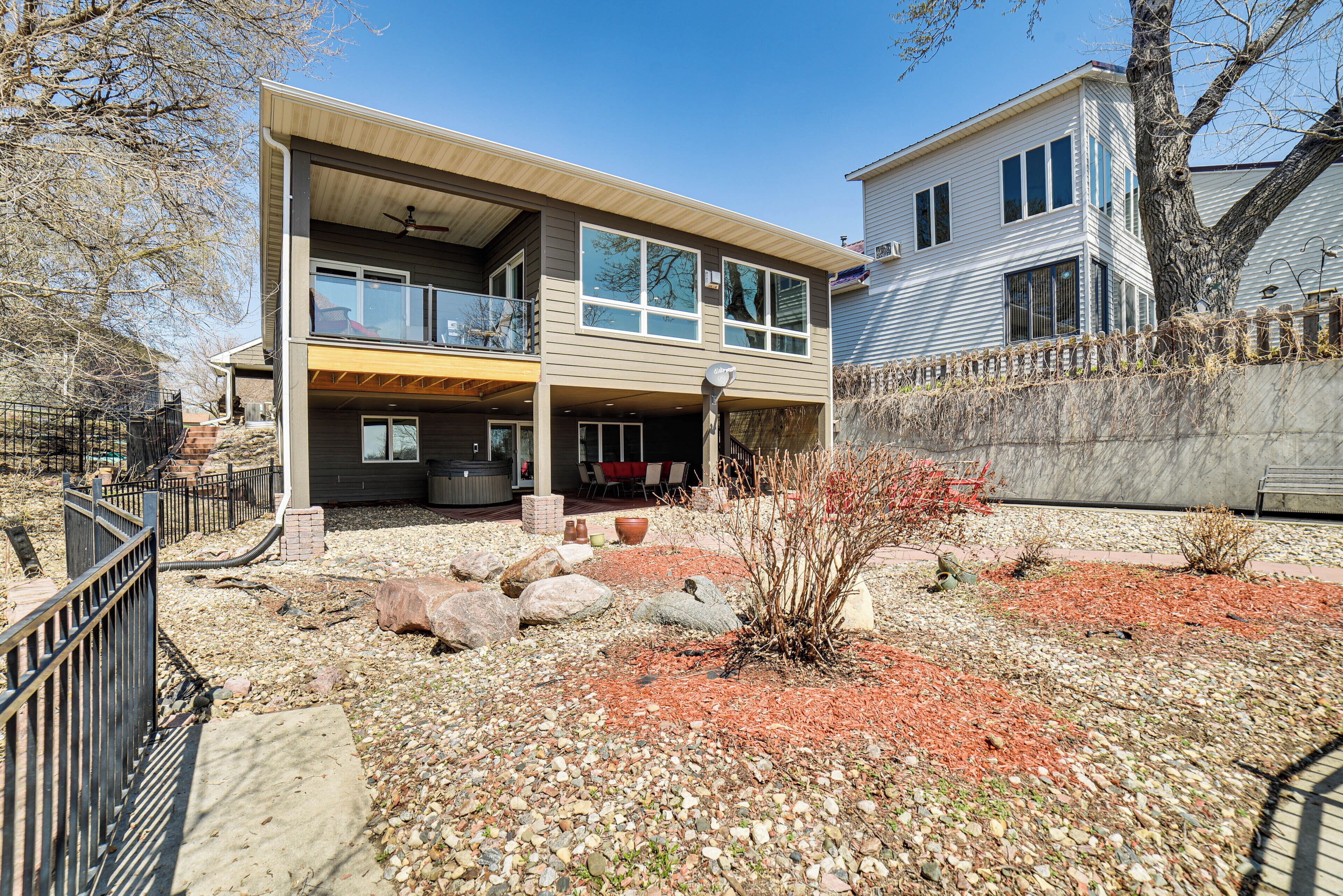 A modern two-story house with a covered patio, a stone pathway, and a small garden area with rocks and sparse vegetation.